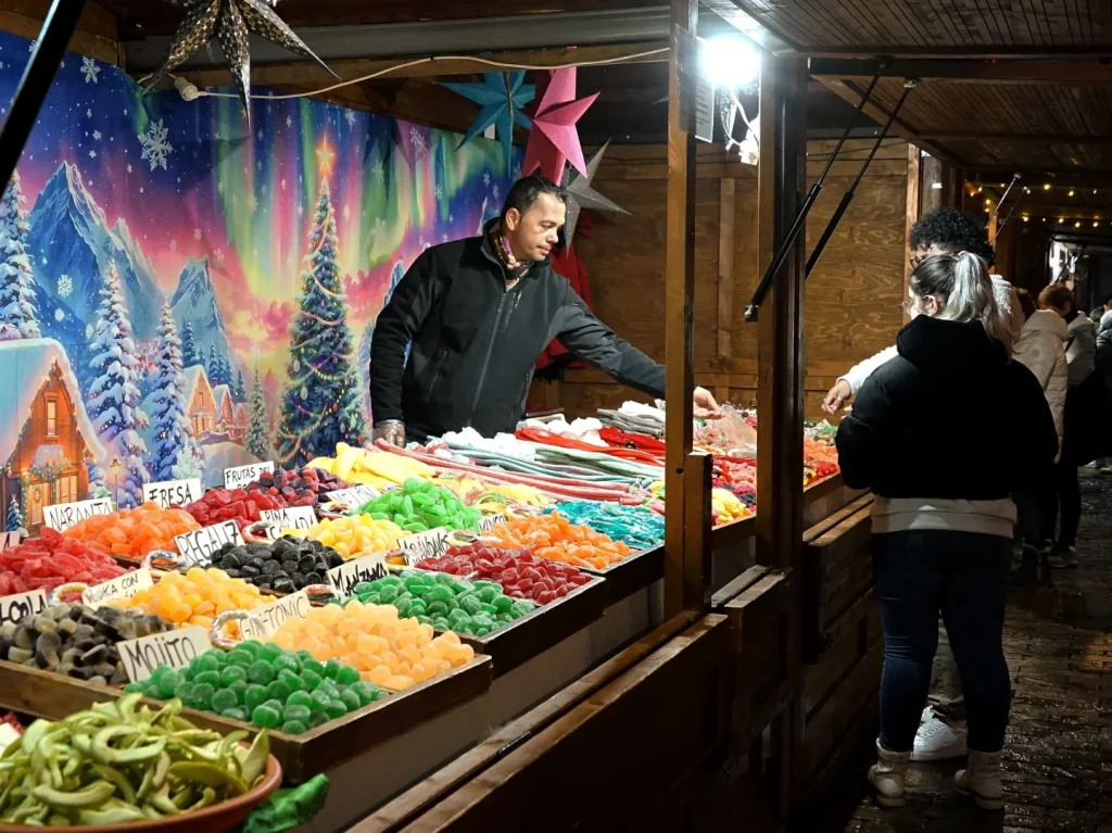 Puesto de dulces de colores y visitantes del mercado navideño