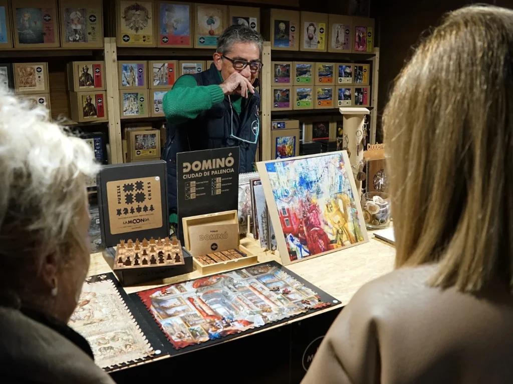 Artesano mostrando juegos y piezas inspiradas en Palencia a varias visitantes